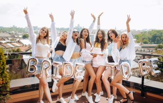Hen Do Group Getaway: Hen Dos Done Right Style, Fun & a Little Sparkle 5 Group of women celebrating a hen do on a rooftop terrace, holding “Bride to Be” balloons and cheering together in a city setting.