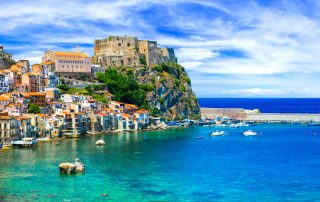 Italy Group Travel: Viva Italia — Exploring Italy’s Highlights with Your Group 4 Coastal Italian town with colourful houses built along the shoreline, a hilltop fortress, and clear turquoise sea below.