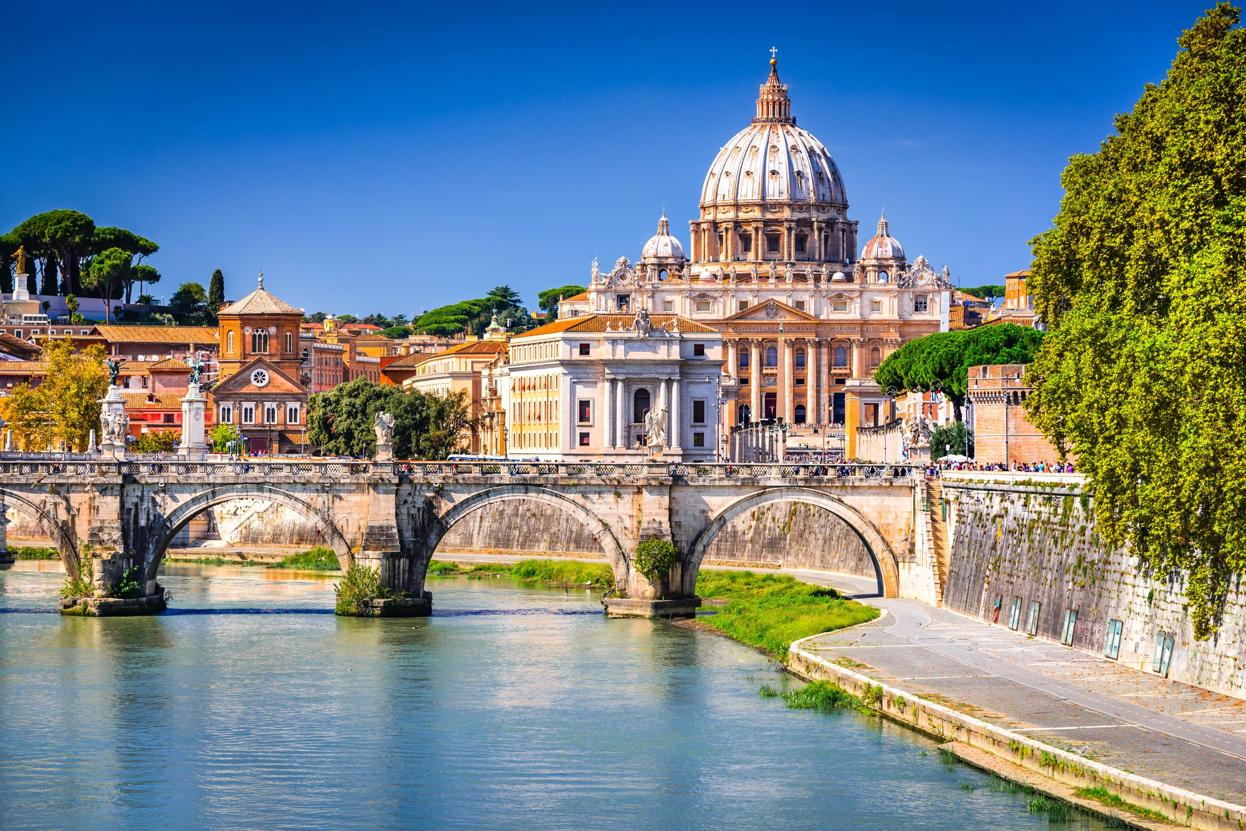 Rome, Italy – Vatican, Saint Peter Basilica and Tiber River View of St Peter’s Basilica and the Tiber River in Rome, with a historic stone bridge and classic Roman architecture in the foreground.