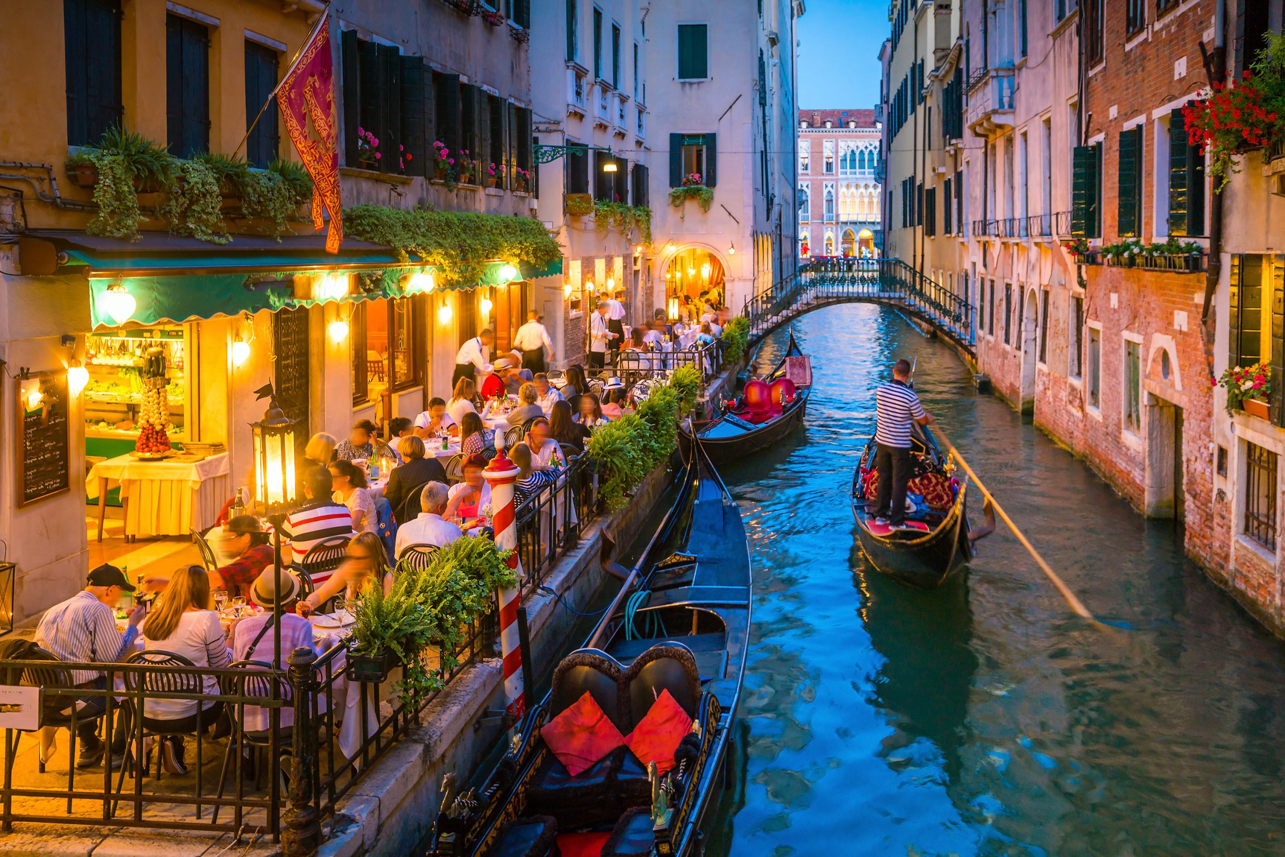 Canal in Venice Italy at night Evening scene in Venice showing gondolas gliding along a canal beside outdoor restaurants and historic buildings lit with warm lights.