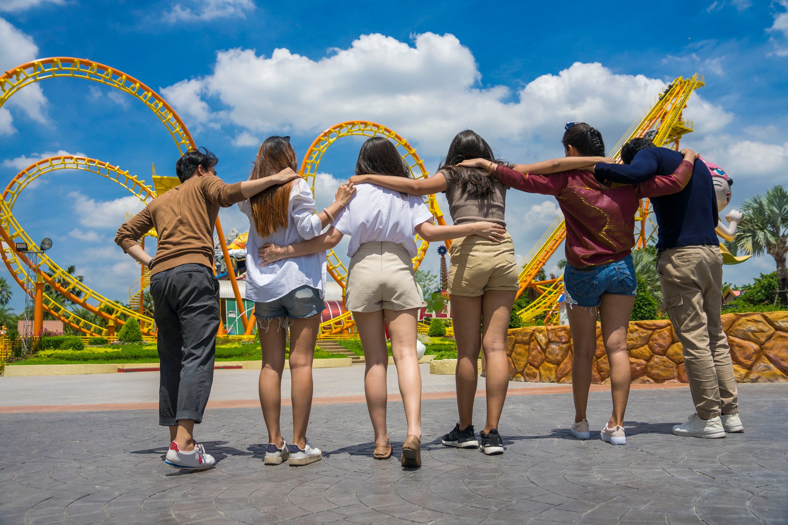 group of happy male and female friends have fun going to an amusement park together in the summer